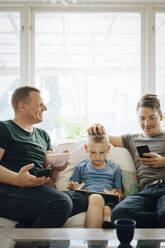 Smiling fathers talking while son using digital tablet at home - MASF20591