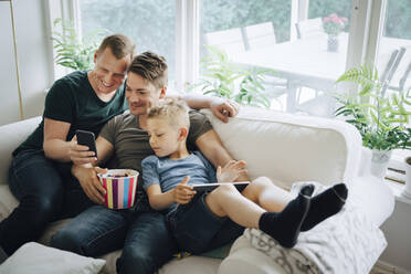 Smiling fathers with son using smart phone on sofa at home - MASF20592