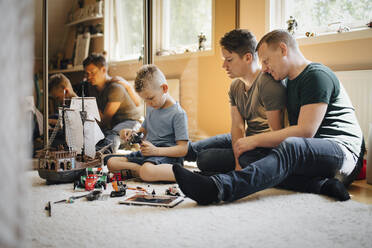 Homosexual fathers looking at son playing while making toy boat at home - MASF20598