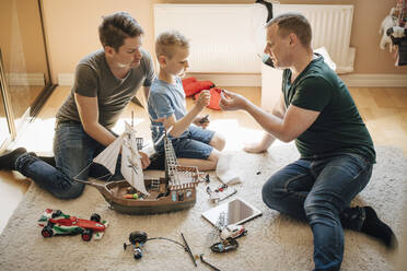Side view of homosexual fathers and son making toy boat at home - MASF20600