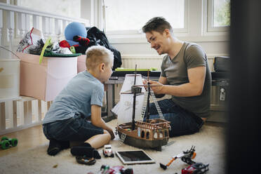Lächelnder Vater und Sohn basteln Spielzeugboot, während sie zu Hause sitzen - MASF20603