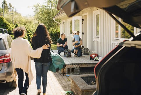 Vater umarmt Sohn, während lesbisches Paar am sonnigen Tag auf das Haus zugeht - MASF20606