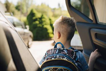 Rückansicht eines Jungen mit Rucksack öffnenden Autos bei sonnigem Wetter - MASF20613