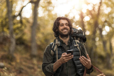 Lächelnder Mann mit Smartphone beim Wegschauen im Wald - MASF20670