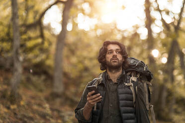 Betrachtender Mann mit Smartphone beim Wegschauen im Wald - MASF20672