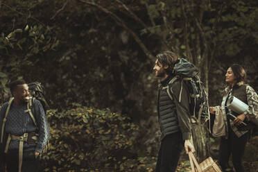 Lächelnde Freunde mit Rucksack unterhalten sich während einer abenteuerlichen Reise im Wald - MASF20673