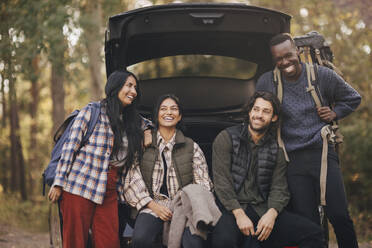 Smiling male and female friends sitting in car trunk during vacation - MASF20680