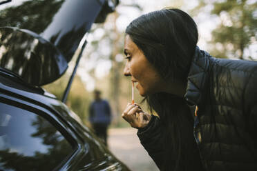 Side view of woman applying lipstick while looking in car window - MASF20691