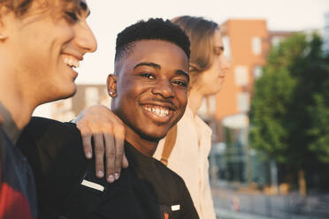 Porträt eines lächelnden jungen Mannes mit Freunden in der Stadt stehend - MASF20710