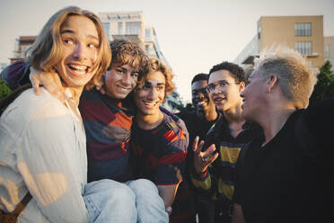 Lächelnde Freunde tragen einen Teenager, während sie in der Stadt stehen - MASF20714