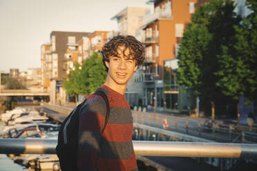 Lächelnder Teenager zwinkert bei Sonnenuntergang auf einer Brücke in der Stadt - MASF20717