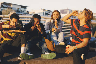 Young and teenage male friends eating pizza at harbor in city - MASF20722