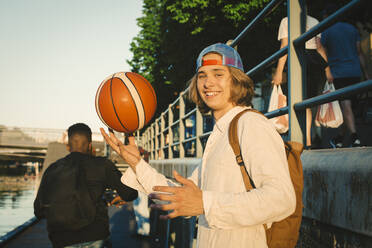 Porträt eines glücklichen Teenagers mit Basketball von einem Freund am Hafen - MASF20734