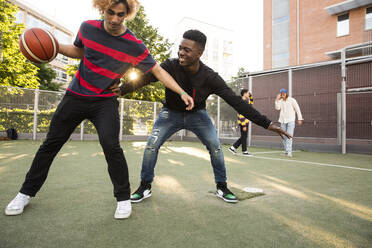 Young man taking basketball from male friend while playing in sports field - MASF20749