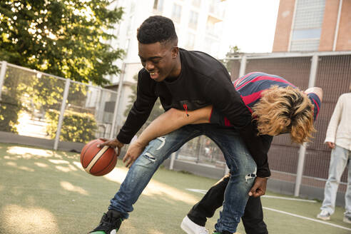 Junger Mann nimmt einem Freund den Basketball weg, während er auf dem Sportplatz spielt - MASF20751
