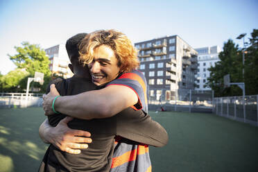 Happy friends embracing each other while playing in sports field - MASF20757