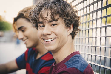 Portrait of smiling teenager with male friend sitting in city - MASF20764