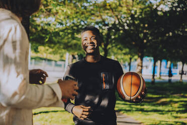 Lächelnder junger Mann mit Teenager-Freund hält Fussball im Park - MASF20786