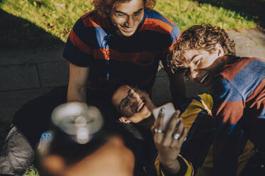 High angle view of smiling male friends using mobile phone in public park - MASF20787