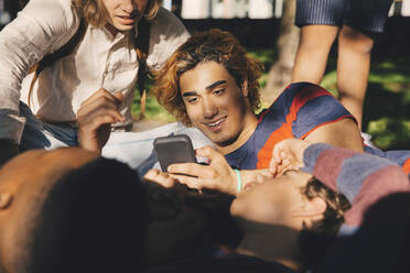 Lächelnder Mann benutzt Smartphone, während er sich mit Freunden im Park vergnügt - MASF20792