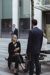 Lächelnde Unternehmerin mit Sandwich im Gespräch mit Mitarbeiterin in der Stadt - MASF20832