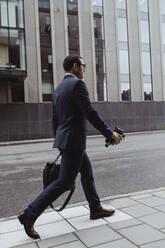 Side view of businessman with bag walking on sidewalk in city - MASF20853