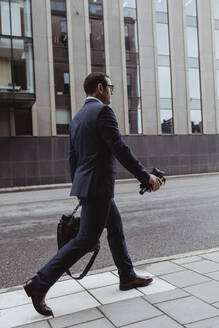 Seitenansicht eines Geschäftsmannes mit Tasche auf dem Bürgersteig in der Stadt - MASF20853