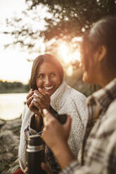 Smiling female friends talking while drinking coffee in forest - MASF20910