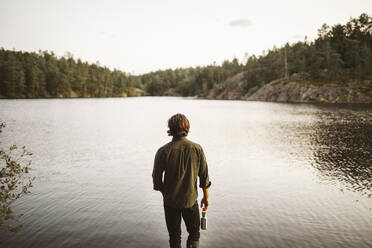 Rückansicht eines Mannes, der während eines Urlaubs am See im Wald steht - MASF20914