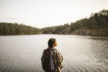Rückansicht einer Frau mit Rucksack an einem See im Wald stehend - MASF20916