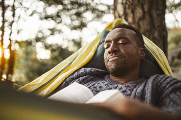 Man with book sleeping in hammock at forest - MASF20929