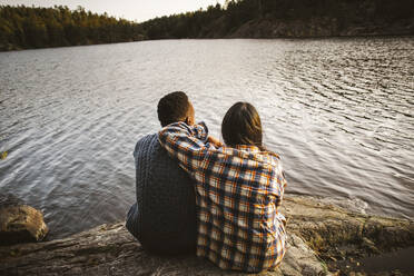 Rear view of man and woman sitting by lake in forest - MASF20935