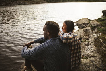 Seitenansicht eines Mannes und einer Frau, die am See im Wald sitzen - MASF20936