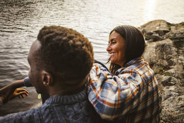 Side view of smiling woman and man sitting by lake in forest - MASF20938