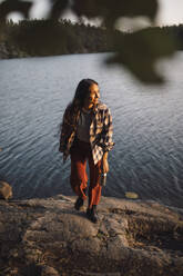 Smiling woman looking away against lake in forest - MASF20939