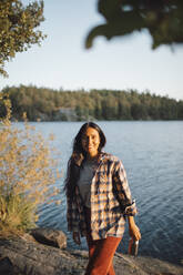 Porträt einer lächelnden Frau mit Flasche gegen einen See im Wald - MASF20940