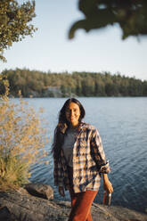 Portrait of smiling woman with bottle against lake in forest - MASF20940