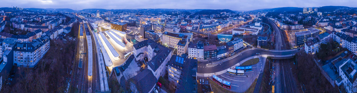 Germany, North Rhine-Westphalia, Wuppertal, Panorama of Wuppertal Hauptbahnhof railroad station and surrounding city buildings at dusk - SKAF00149