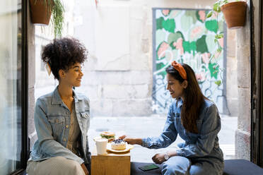 Friends having food and drink while sitting by window at cafe - VABF03912