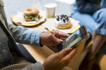 Mittlere erwachsene Frau, die ein Mobiltelefon benutzt, während sie mit einem Freund in einem Café sitzt - VABF03914