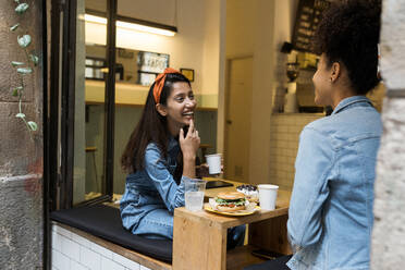 Lächelnde Frauen, die sich am Fenster eines Cafés unterhalten - VABF03919
