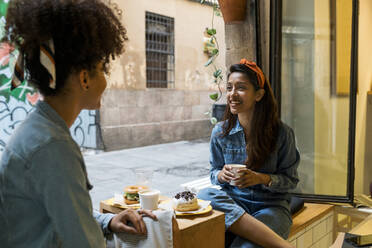 Friends smiling while having food and drink sitting at cafe - VABF03920