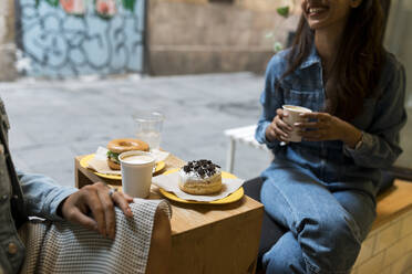 Freunde sitzen bei Kaffee und Essen am Fenster eines Cafés - VABF03921