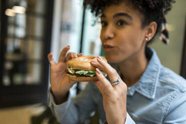 Mid adult woman eating burger while sitting at cafe - VABF03922