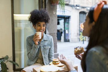 Weibliche Freunde unterhalten sich bei Essen und Trinken am Fenster eines Cafés - VABF03924