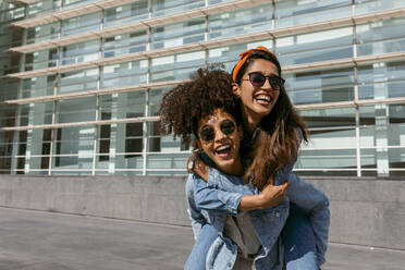 Mid adult woman piggybacking woman while standing on rooftop against building - VABF03937