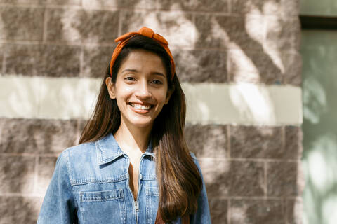 Young woman smiling while standing against wall stock photo