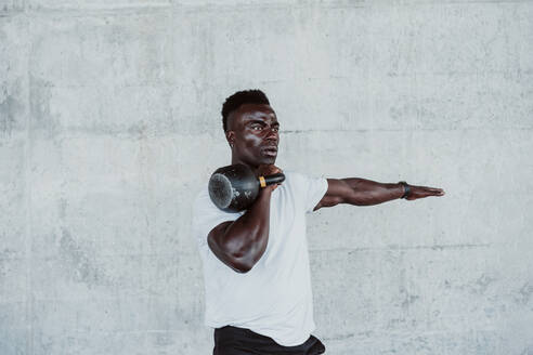 Young male athlete exercising with kettle bell against white wall - EBBF01336