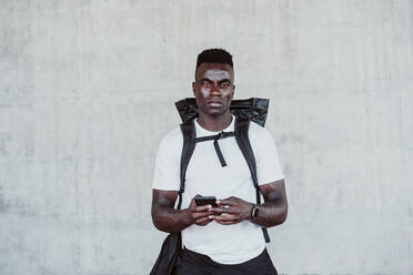 Ernsthafter Sportler, der sein Smartphone hält, während er an einer weißen Wand steht - EBBF01346