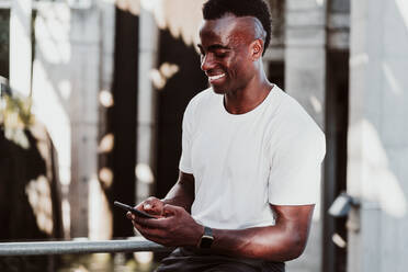 Lächelnder Sportler mit Textnachrichten auf dem Smartphone sitzend - EBBF01356